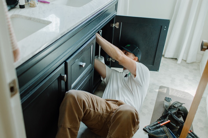 Benny working under a bathroom vanity on the plumbing in Kalamazoo, MI